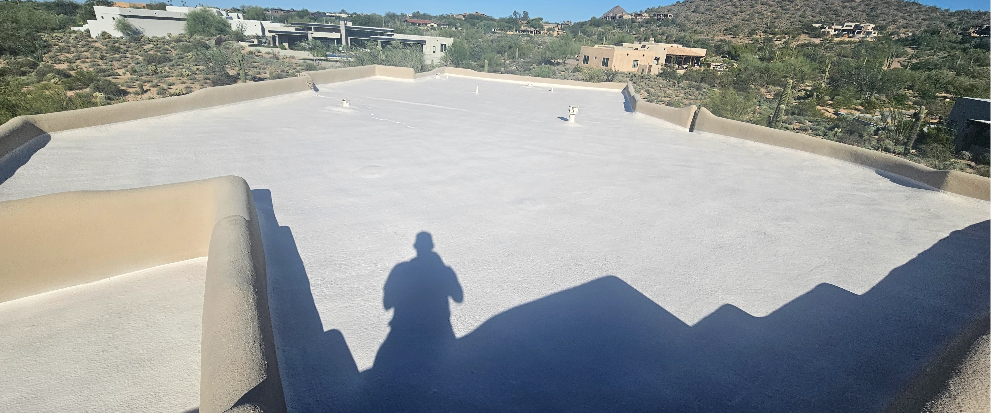 White foam roof recoat on a Phoenix flat-roof home, showing vents and desert landscape