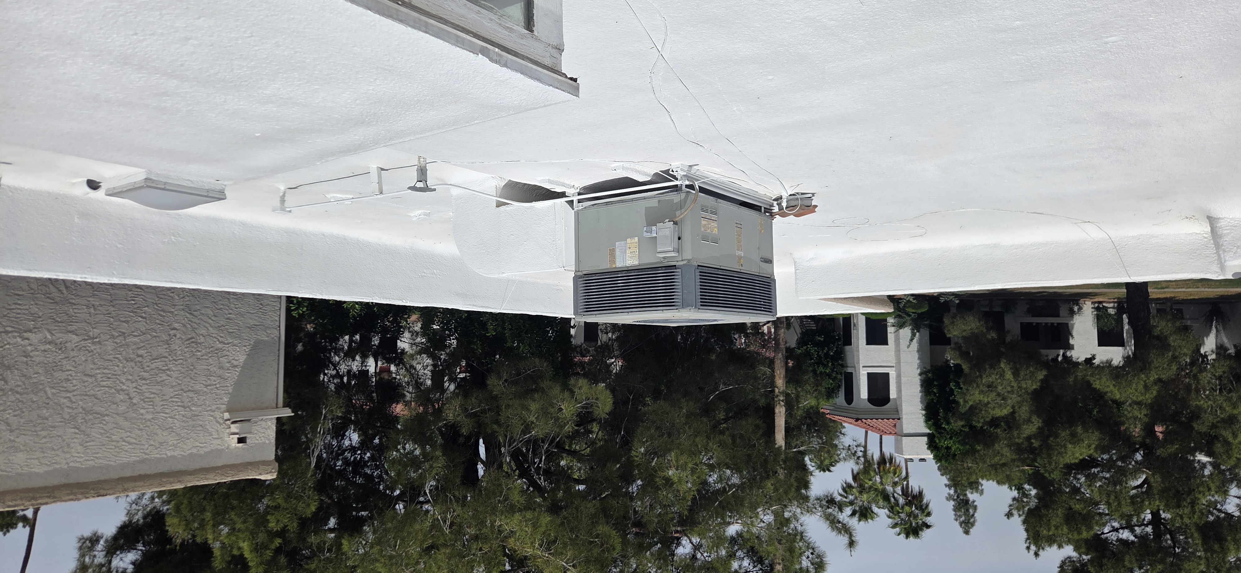 A newly installed white foam roof with an HVAC unit sits on a commercial building in Phoenix, surrounded by green trees.