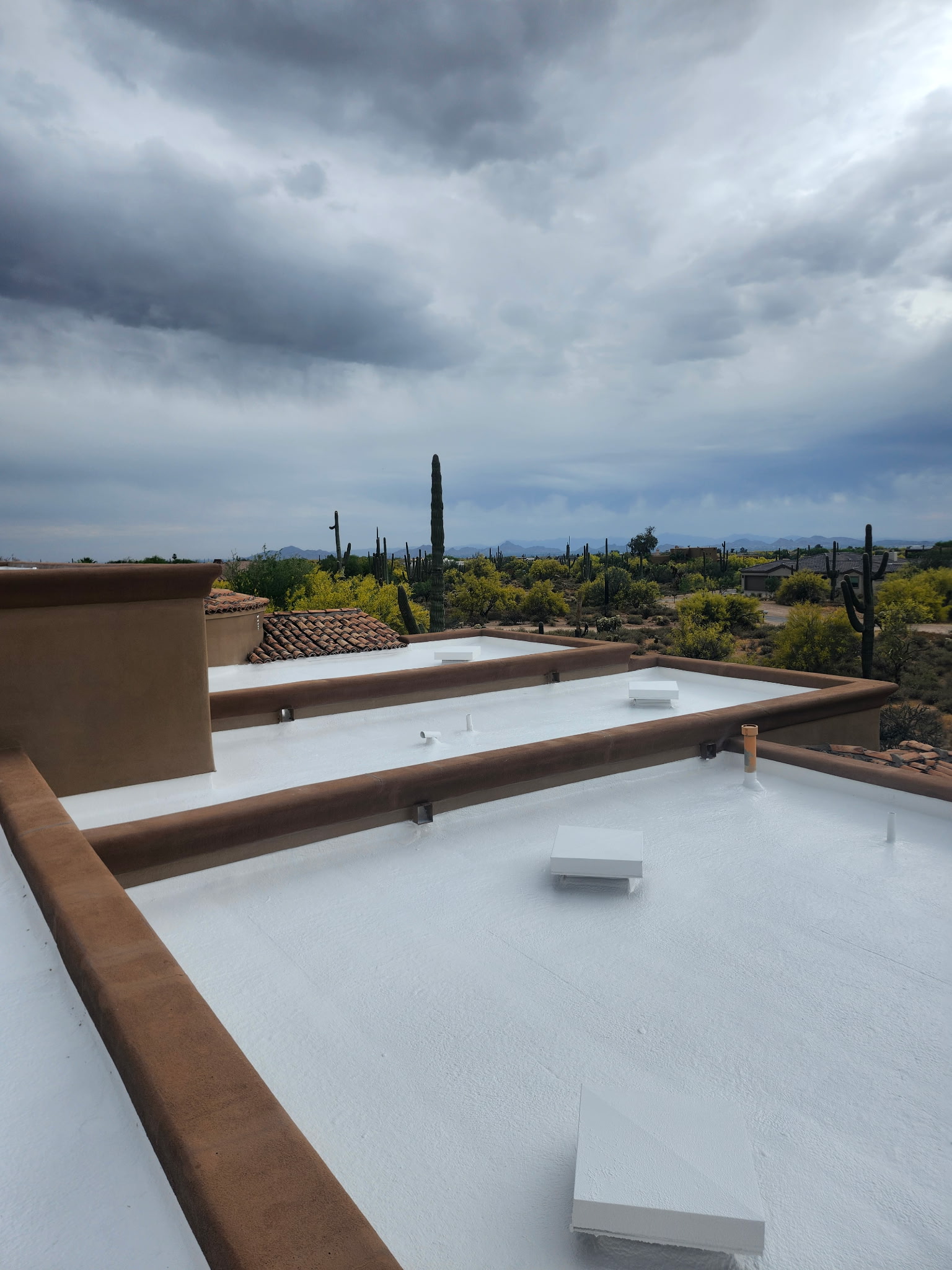 A newly installed white foam flat roof on a home in a desert landscape with saguaros under a cloudy sky.