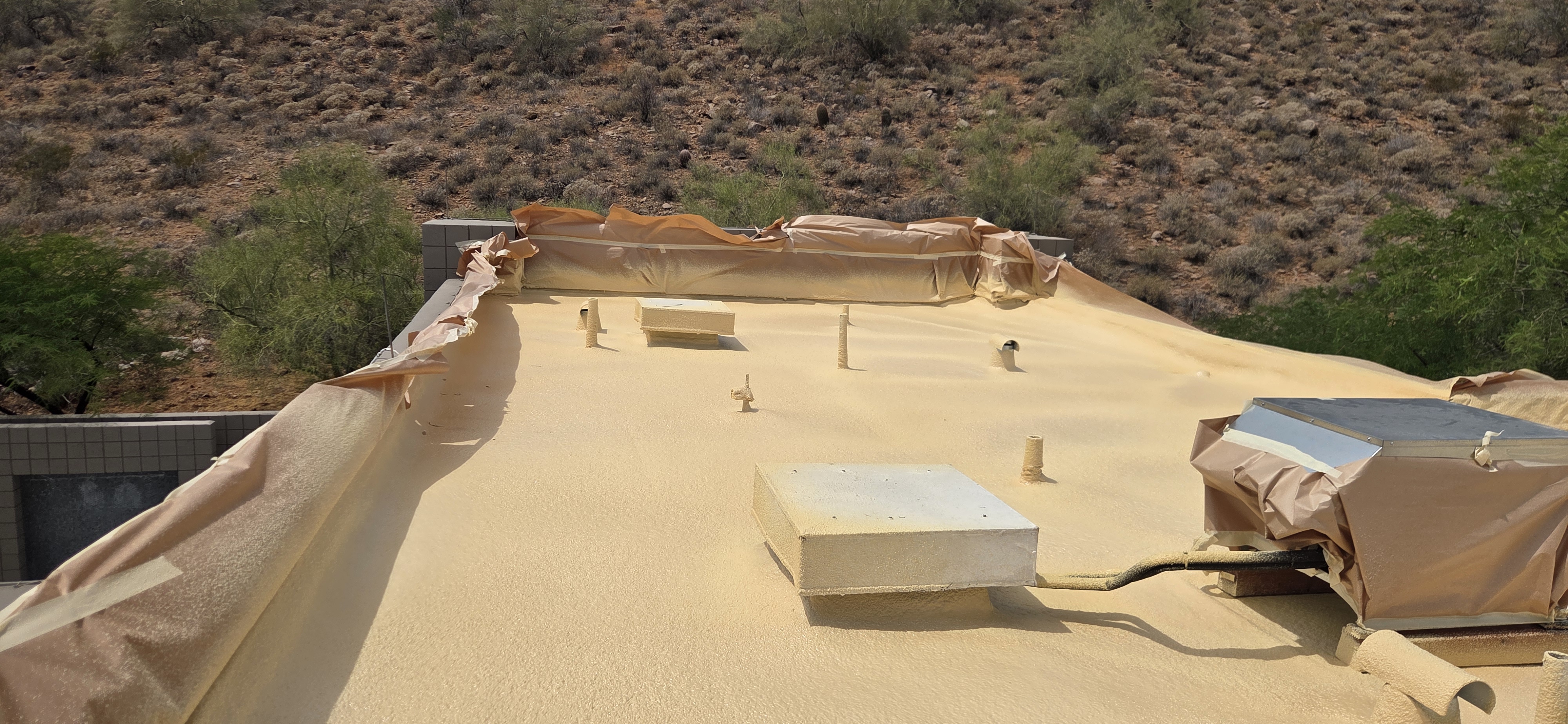Newly installed foam roof on a flat residential building in Phoenix with desert hills in the background.