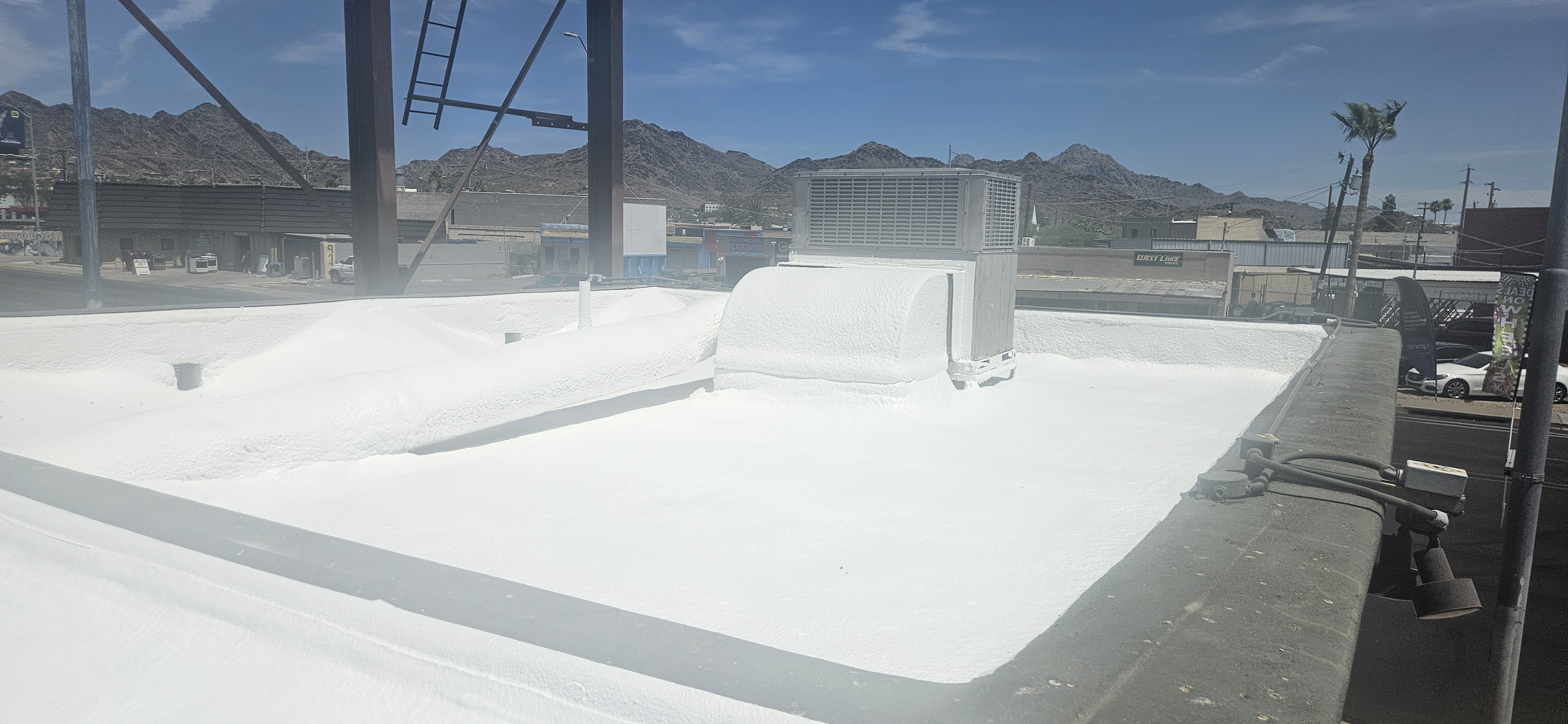 A newly applied white foam roof covers a flat commercial building, with ventilation units and pipes integrated into the smooth surface, under a bright Phoenix sky.