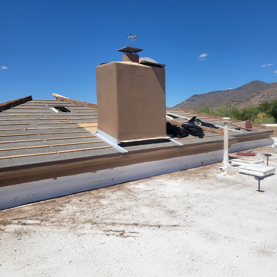 A close-up view of a residential roof in Carefree undergoing tile repair, with exposed underlayment and a flat roof section.