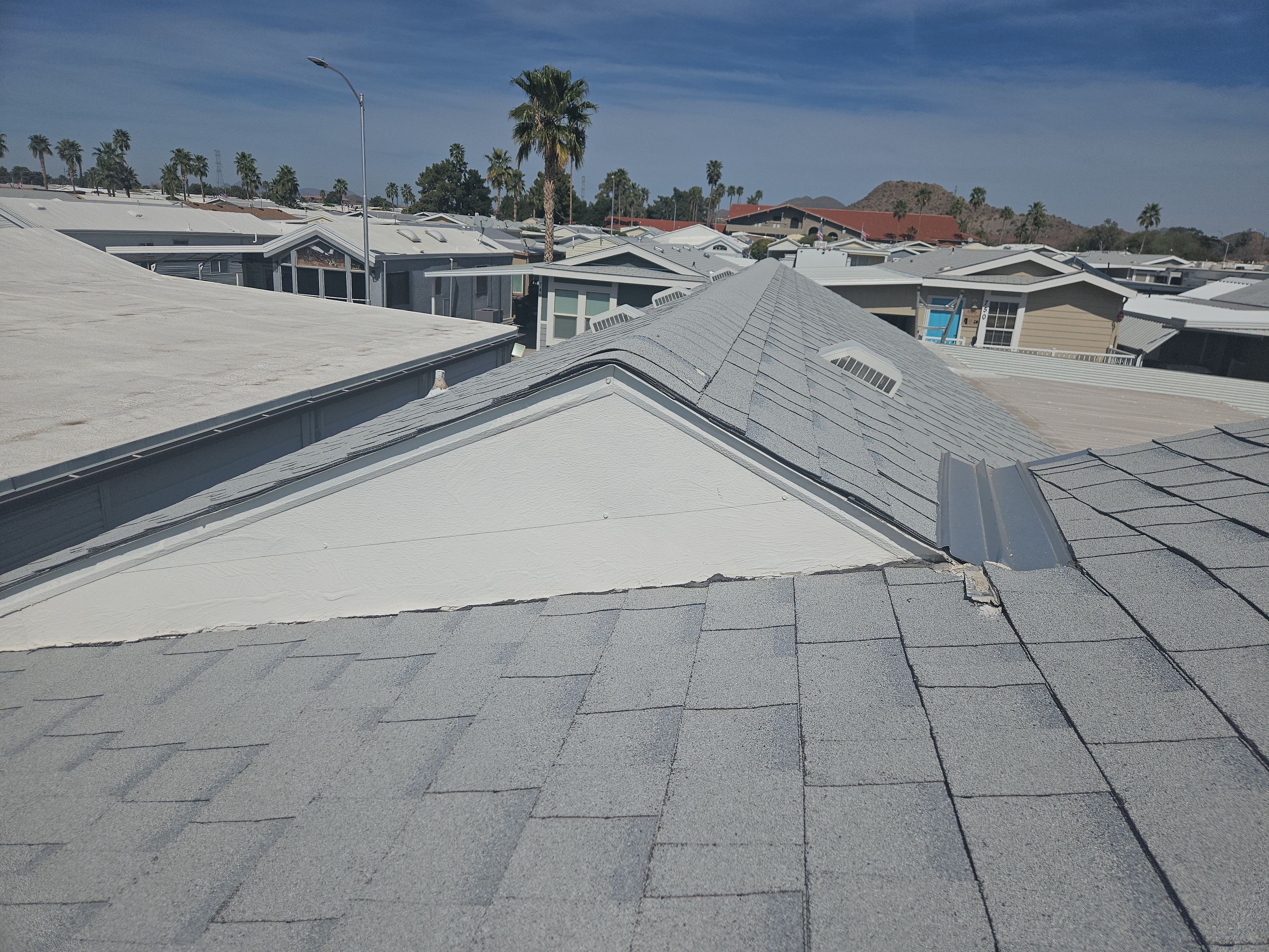 An aerial view showcases light gray shingle roofs with white flat roof sections at a mobile home park on a sunny day in Phoenix.