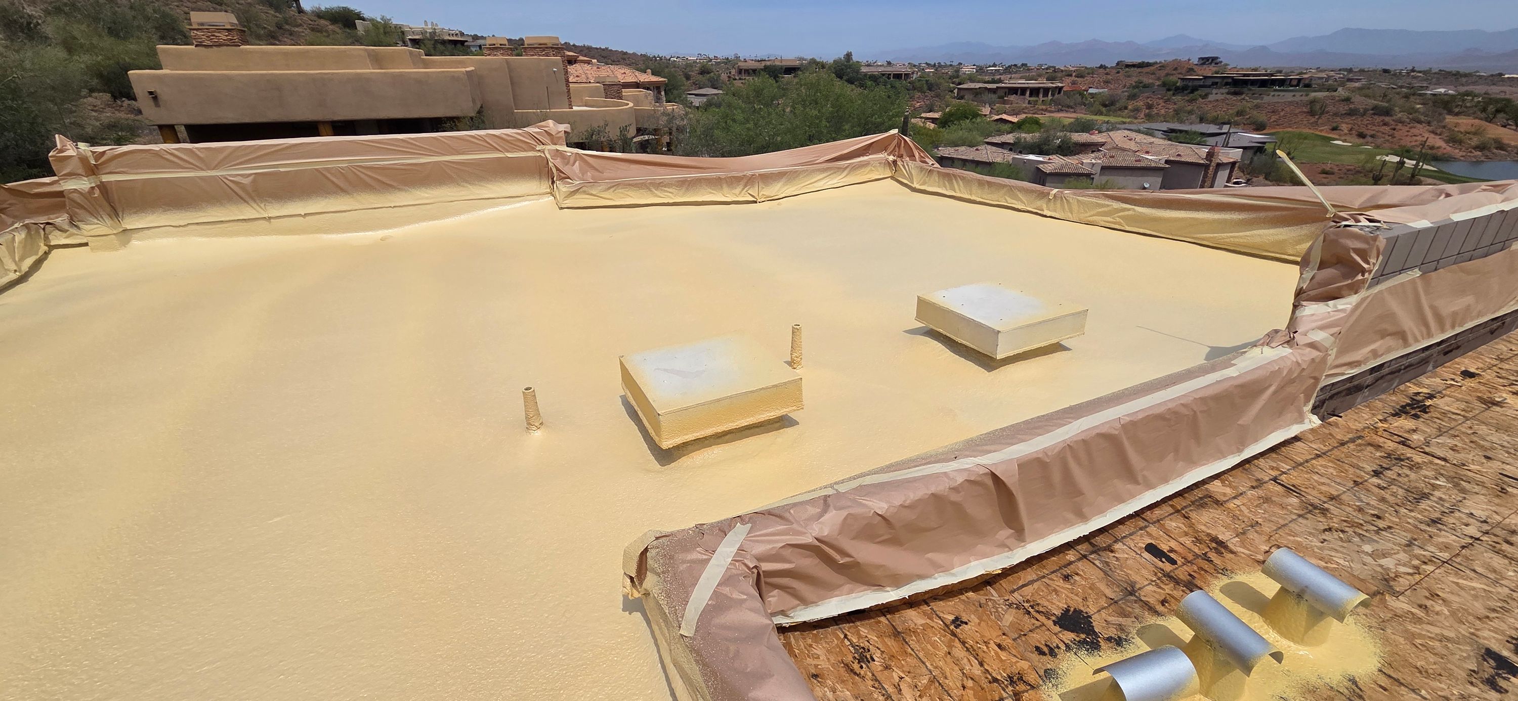 A newly applied light yellow spray foam roof on a flat residential building in Phoenix with desert landscaping in the background.