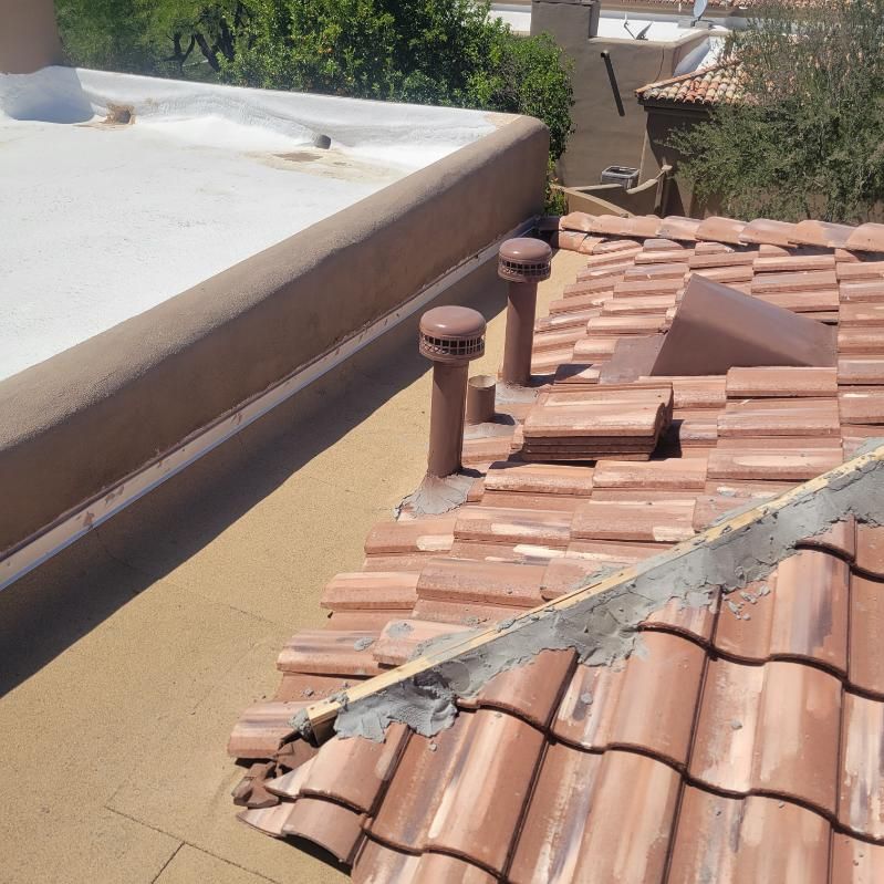 Close-up shows a detail on a flat roof with a light coating next to reddish-brown tile roofing.