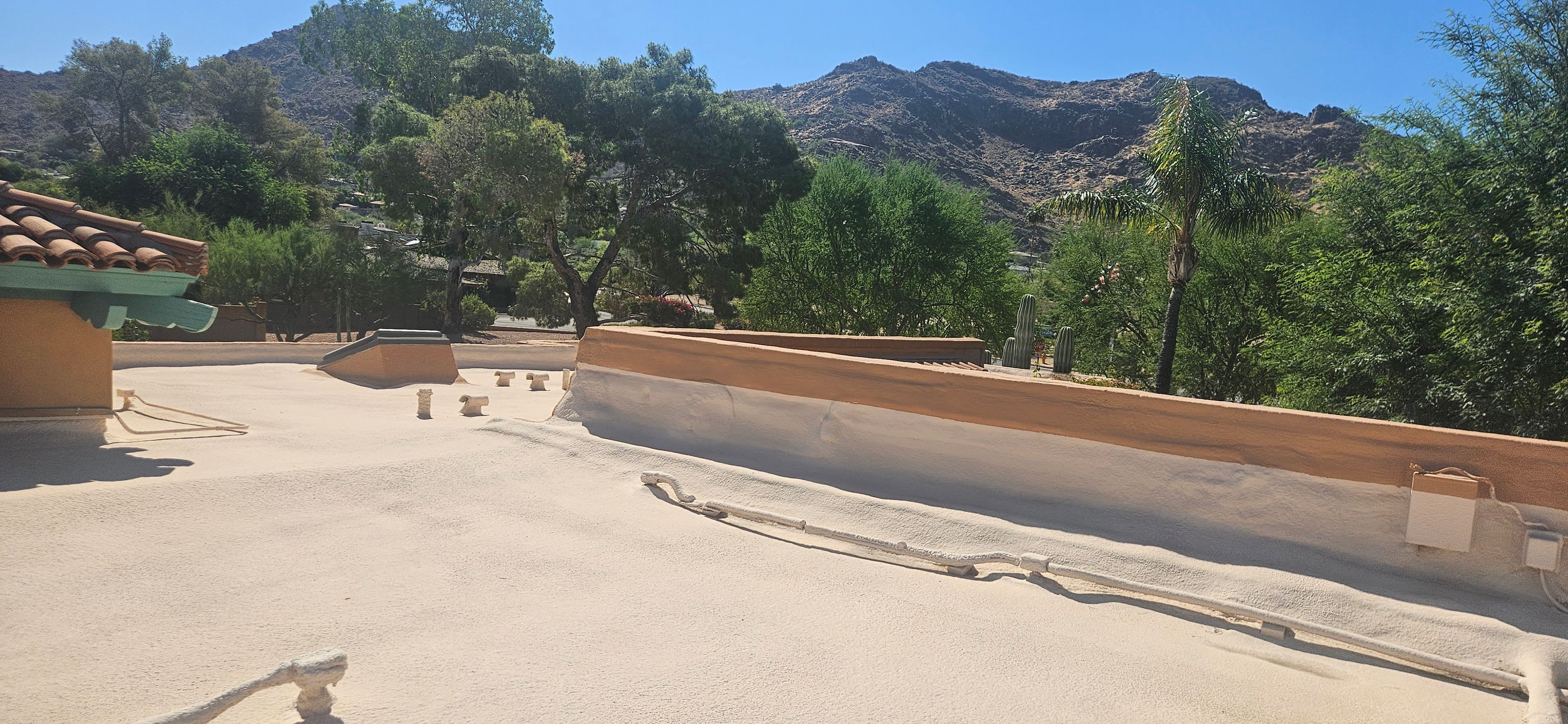 Newly installed light-colored foam roof on a flat residential building with mountains and trees in the background.